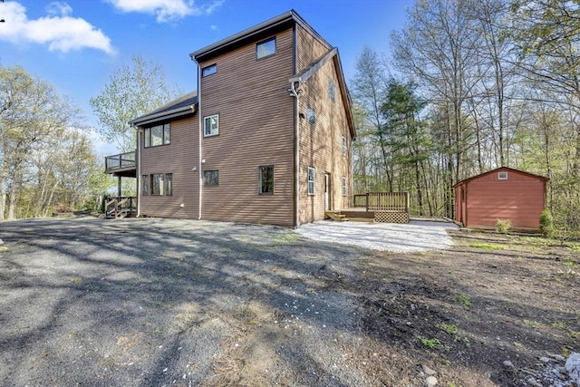 back of property with an outdoor structure, a wooden deck, and a storage unit