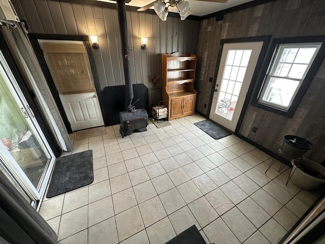 foyer with light tile patterned floors, wood walls, ceiling fan, and a wood stove