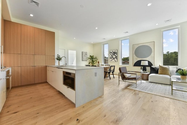 kitchen featuring light wood finished floors, visible vents, modern cabinets, a peninsula, and a sink