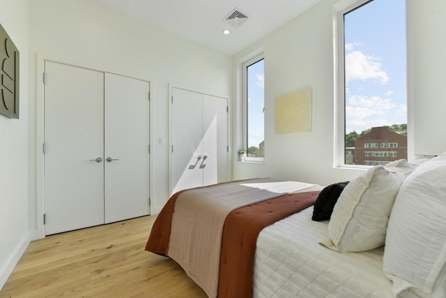 bedroom with multiple closets, light wood-type flooring, visible vents, and recessed lighting