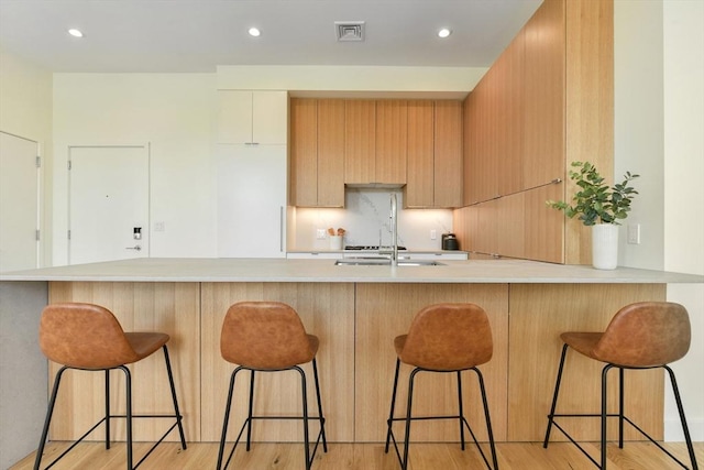 kitchen with light wood finished floors, light countertops, visible vents, a sink, and a peninsula