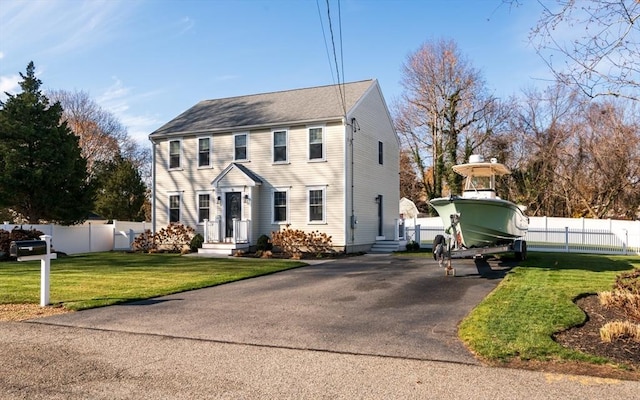 colonial inspired home featuring driveway, fence, and a front lawn