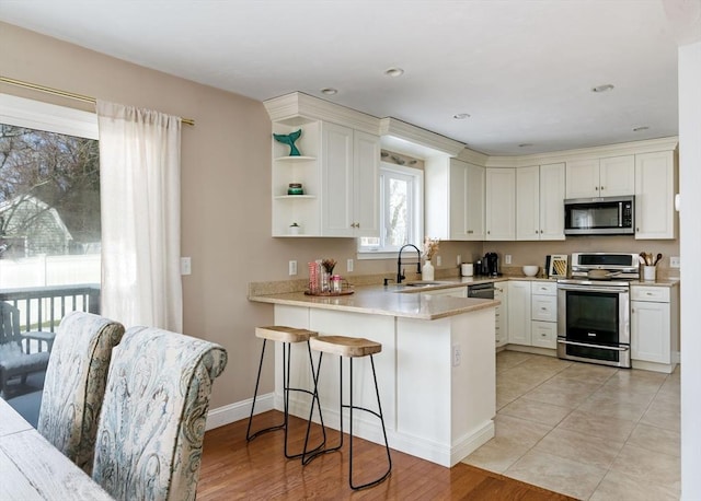 kitchen with stainless steel appliances, a peninsula, a sink, light countertops, and open shelves