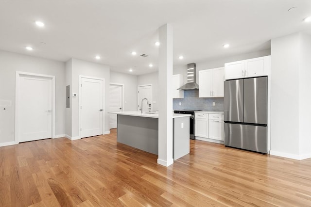 kitchen featuring range with electric cooktop, light countertops, wall chimney range hood, freestanding refrigerator, and an island with sink