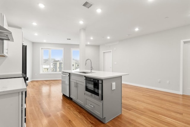 kitchen featuring a sink, visible vents, light countertops, gray cabinets, and a center island with sink