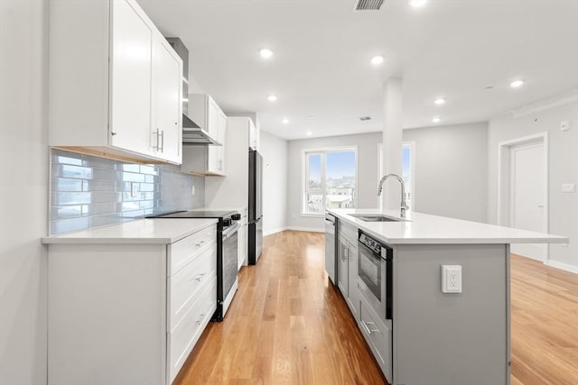 kitchen with stainless steel appliances, a sink, white cabinetry, light countertops, and an island with sink