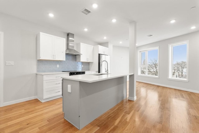 kitchen with a sink, visible vents, light countertops, wall chimney exhaust hood, and a center island with sink