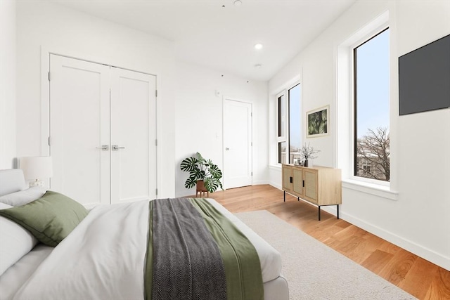 bedroom with light wood finished floors, a closet, recessed lighting, and baseboards