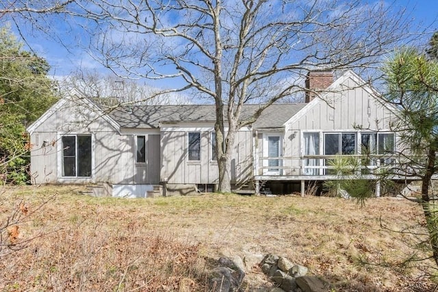 back of house featuring a deck, a shingled roof, board and batten siding, and a chimney