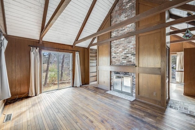 unfurnished living room featuring beamed ceiling, a fireplace, visible vents, wood walls, and hardwood / wood-style floors