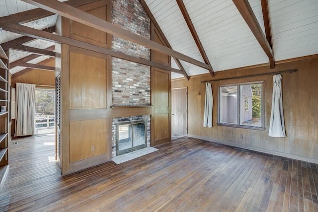 unfurnished living room with wooden ceiling, wood-type flooring, beam ceiling, wooden walls, and a fireplace with flush hearth