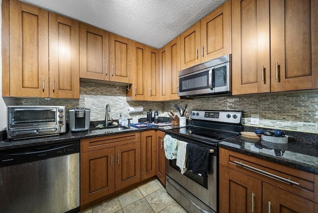 79 Poplar St Unit 10, Boston, MA 02131 - kitchen featuring stainless steel appliances, a sink, brown cabinets, tasteful backsplash, and dark stone counters