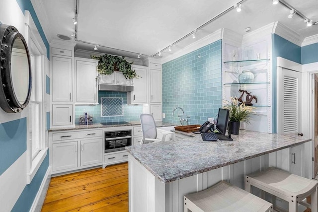 8 S St, Dennis, MA 02639 - kitchen with rail lighting, stainless steel oven, a peninsula, light wood-style flooring, and crown molding