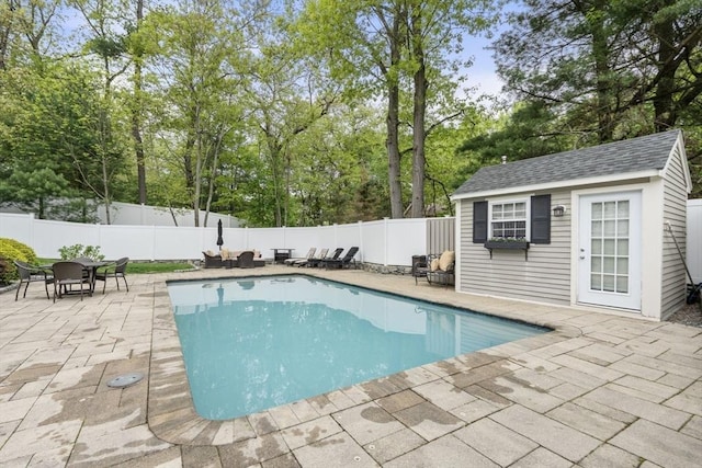 view of pool featuring a patio area, a fenced backyard, an outdoor structure, and view of scattered trees