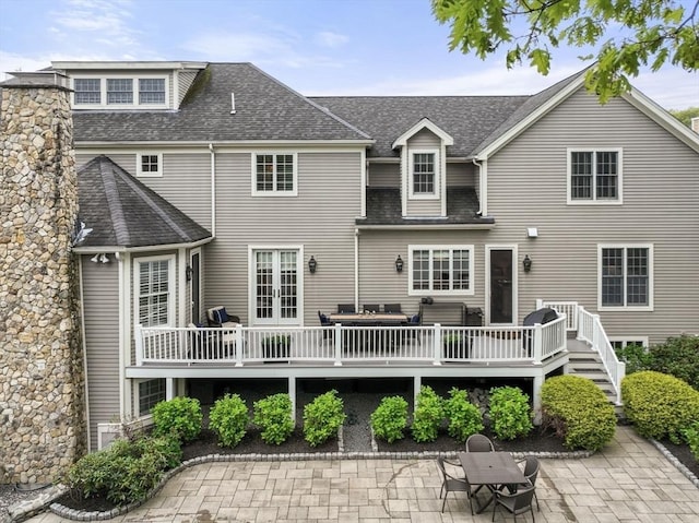 rear view of property with a deck, a patio area, and a shingled roof