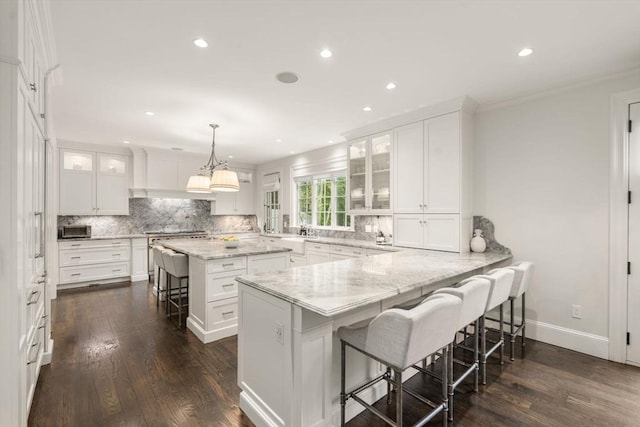 kitchen featuring a kitchen bar, tasteful backsplash, white cabinetry, recessed lighting, and ornamental molding