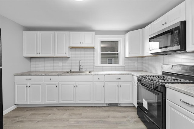 kitchen with light hardwood / wood-style floors, black gas stove, white cabinetry, and sink