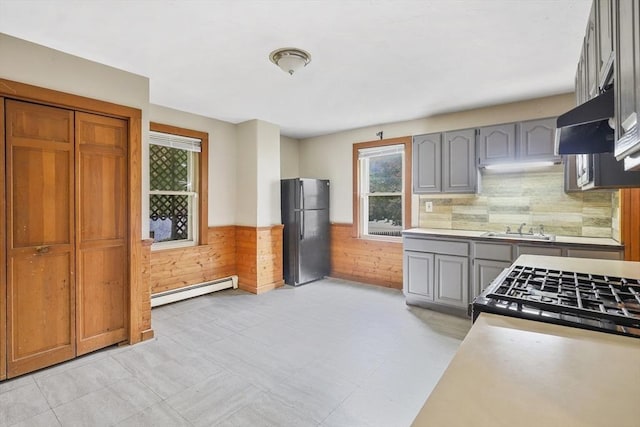 kitchen featuring gray cabinets, black fridge, baseboard heating, and wooden walls