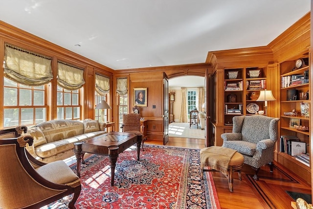 29 Willard Cmn, Concord, MA 01742 - living room featuring light wood-type flooring, ornamental molding, wood walls, built in shelves, and arched walkways