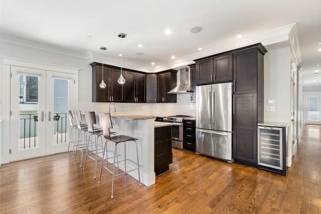 kitchen featuring dark brown cabinetry, beverage cooler, wall chimney range hood, french doors, and appliances with stainless steel finishes