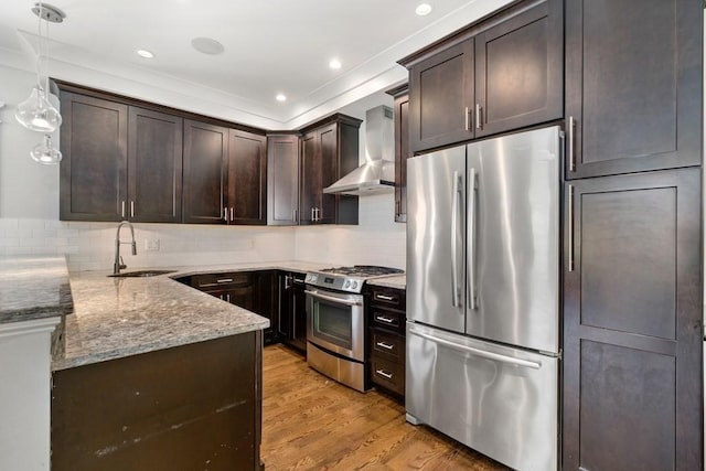 kitchen with dark brown cabinets, wall chimney range hood, light stone counters, a sink, and appliances with stainless steel finishes
