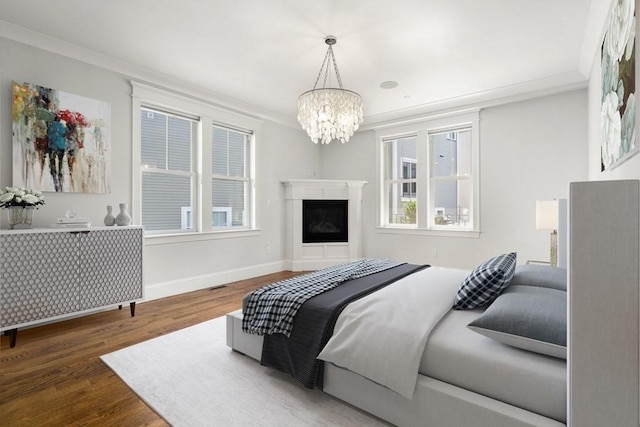 bedroom with crown molding, wood finished floors, a fireplace, baseboards, and a chandelier