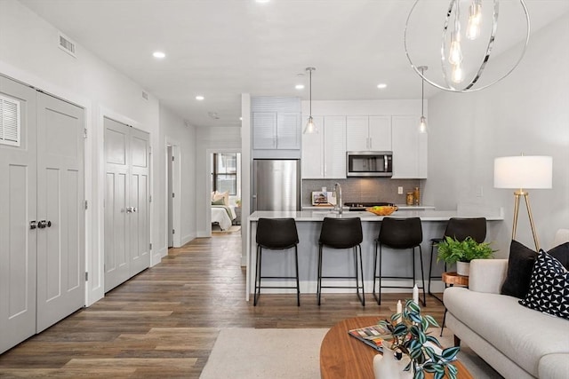 kitchen featuring appliances with stainless steel finishes, a breakfast bar, dark hardwood / wood-style floors, decorative light fixtures, and white cabinets