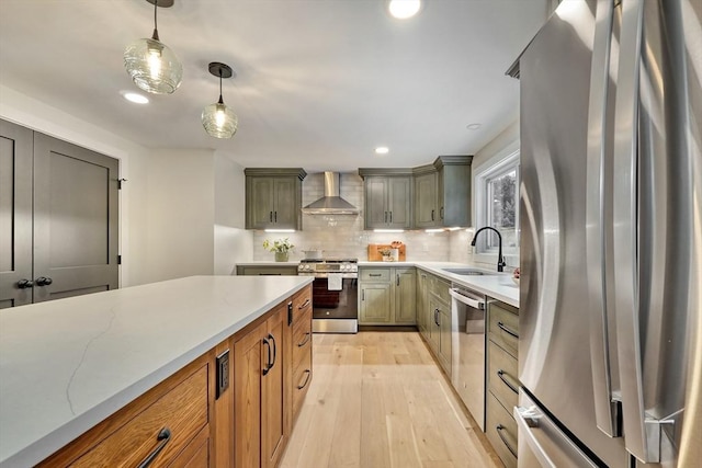 kitchen with sink, appliances with stainless steel finishes, hanging light fixtures, light stone countertops, and wall chimney exhaust hood