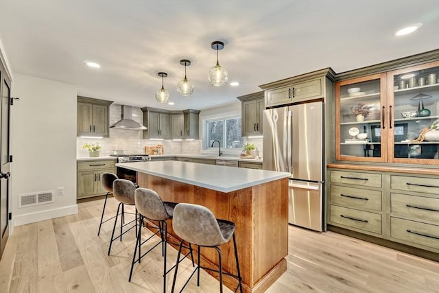 kitchen featuring pendant lighting, wall chimney range hood, light hardwood / wood-style flooring, appliances with stainless steel finishes, and a center island