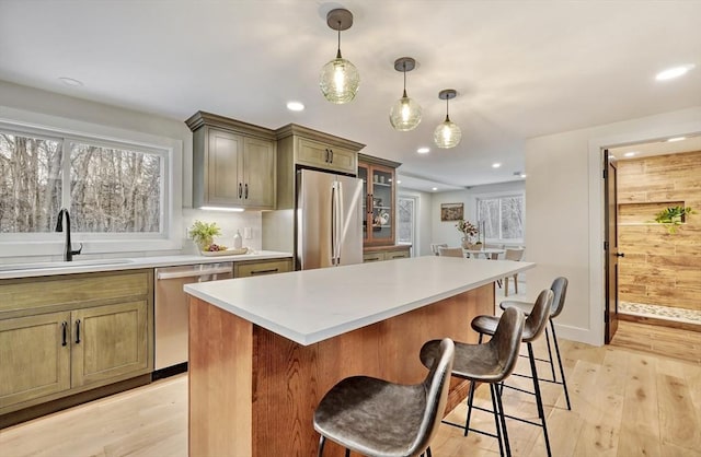 kitchen with sink, appliances with stainless steel finishes, hanging light fixtures, a center island, and light hardwood / wood-style floors