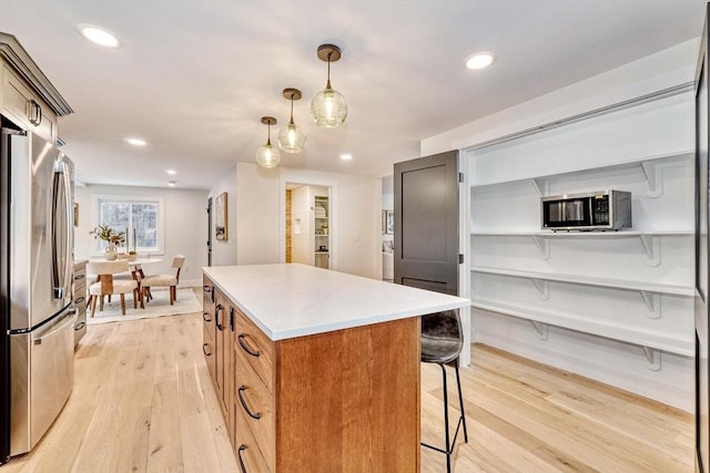 kitchen featuring appliances with stainless steel finishes, decorative light fixtures, a center island, and light hardwood / wood-style floors