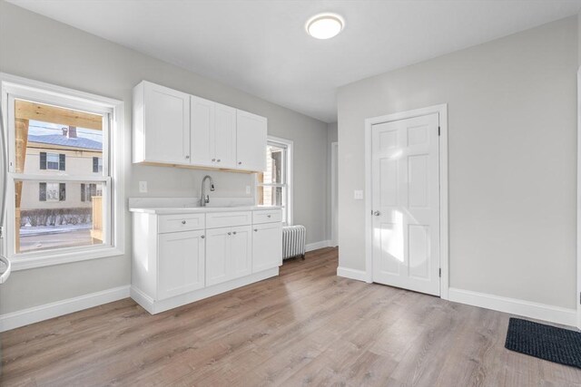 kitchen featuring light countertops, radiator heating unit, white cabinetry, a sink, and light wood-type flooring