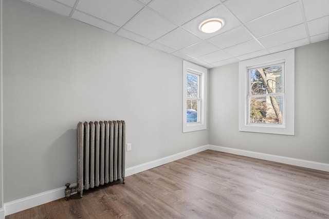 spare room featuring baseboards, wood finished floors, a paneled ceiling, and radiator