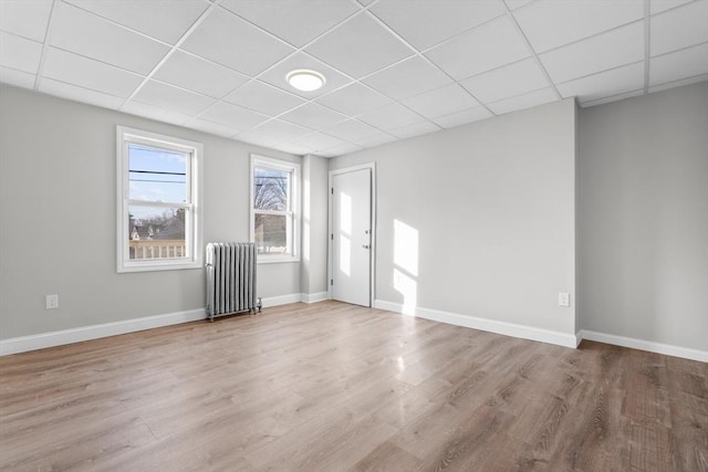 spare room featuring radiator, baseboards, a drop ceiling, and wood finished floors