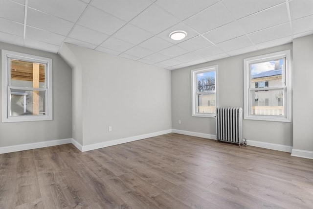 empty room with radiator heating unit, baseboards, and light wood-style flooring