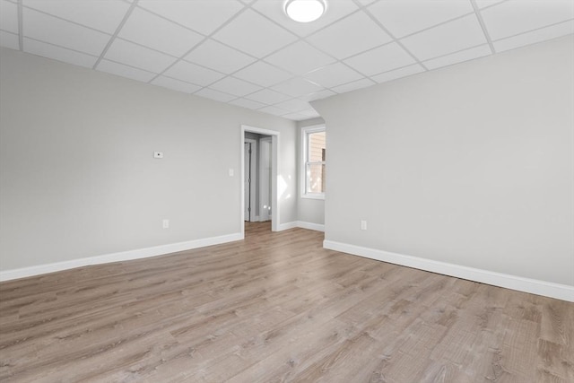 unfurnished room with light wood-type flooring, a drop ceiling, and baseboards