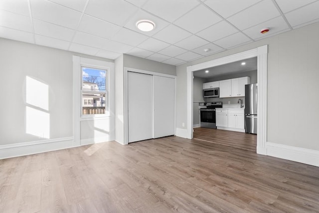 unfurnished living room featuring a paneled ceiling, baseboards, and light wood finished floors