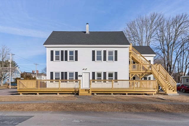 view of front of house featuring stairway, a chimney, a shingled roof, and a deck