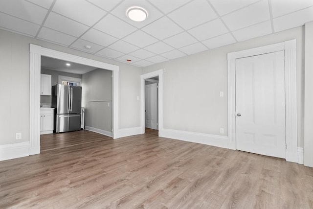 empty room featuring a drop ceiling, light wood-type flooring, and baseboards