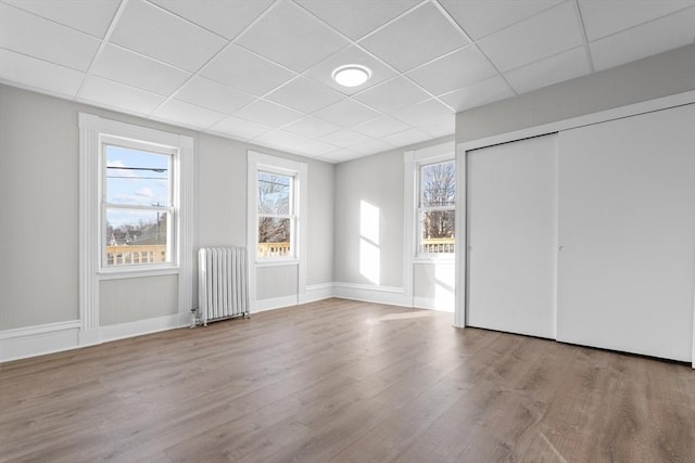 unfurnished bedroom with light wood-style floors, a closet, a paneled ceiling, and radiator