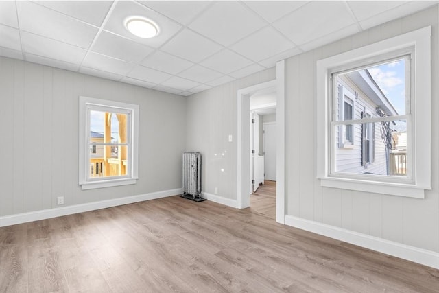 unfurnished room featuring baseboards, a drop ceiling, light wood-style flooring, and radiator heating unit