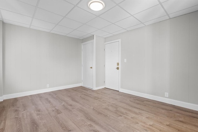 spare room with a paneled ceiling, light wood-style floors, and baseboards