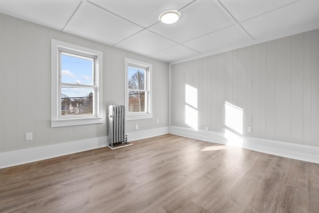 spare room featuring baseboards, radiator heating unit, and light wood-style floors