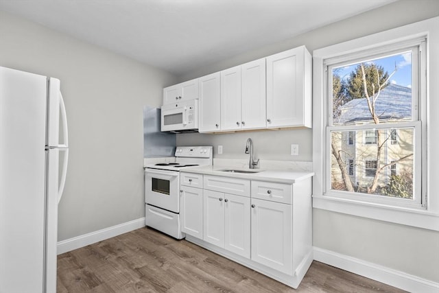 kitchen with white appliances, a sink, white cabinets, light countertops, and light wood-type flooring