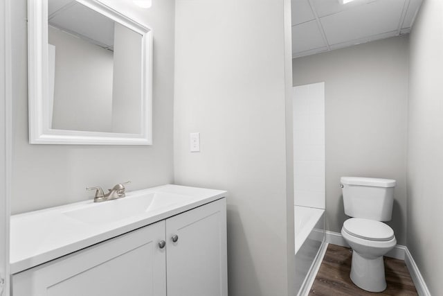 bathroom featuring toilet, vanity, wood finished floors, a drop ceiling, and baseboards