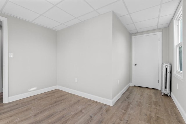 unfurnished room with baseboards, radiator heating unit, a drop ceiling, and light wood-style floors