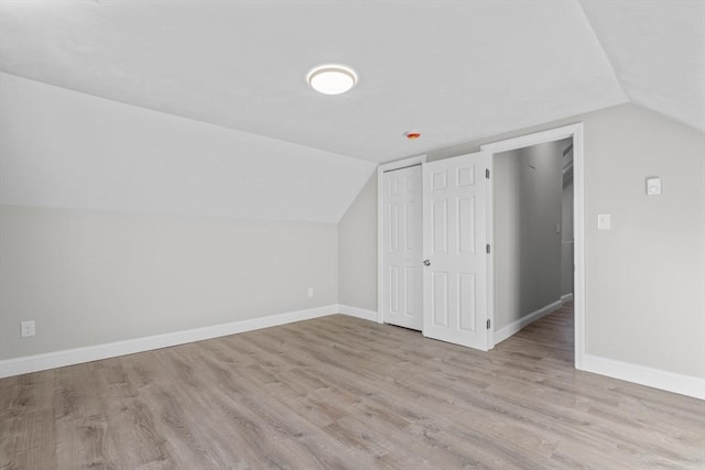 additional living space with light wood-style flooring, baseboards, and vaulted ceiling