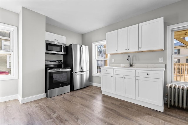 kitchen with light wood-style flooring, stainless steel appliances, a sink, white cabinetry, and radiator heating unit