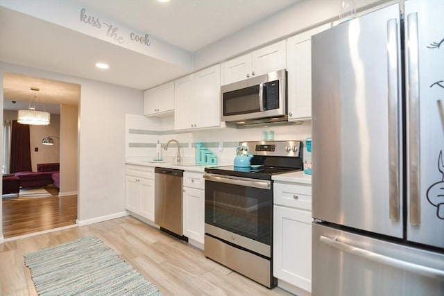 kitchen with white cabinets, light wood-type flooring, stainless steel appliances, and tasteful backsplash