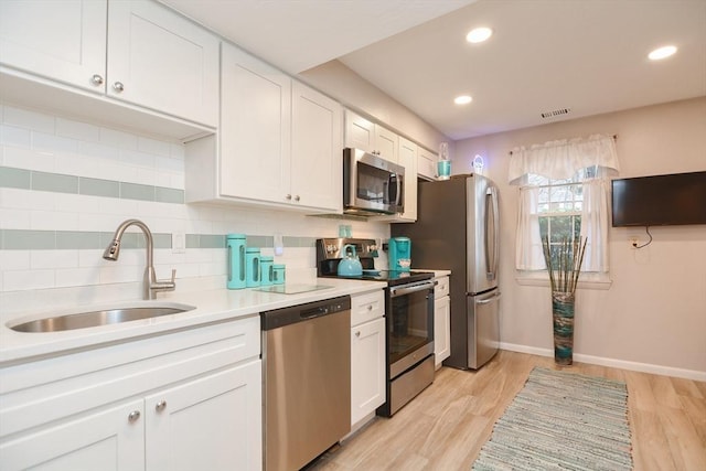 kitchen featuring white cabinets, sink, decorative backsplash, light wood-type flooring, and stainless steel appliances